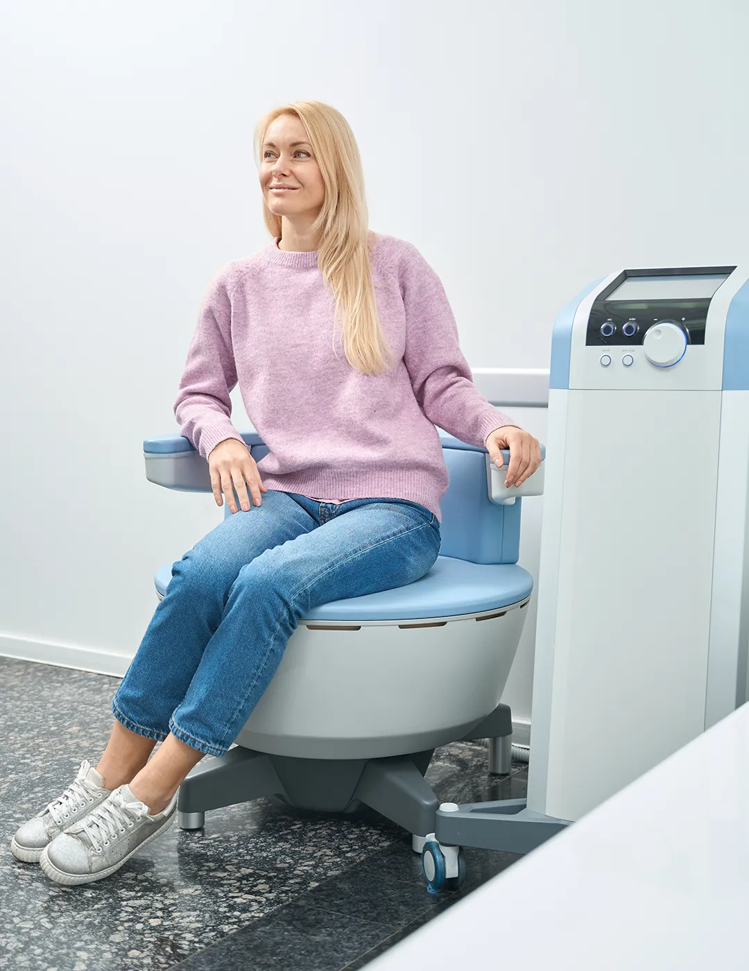 A woman seated on an Emsella machine undergoing treatment.