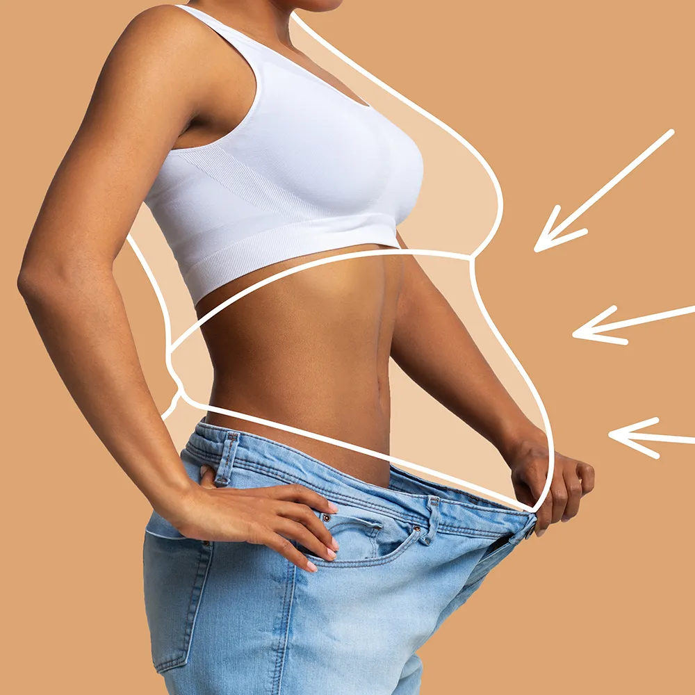 A woman happily looking in the mirror, noticing her pants fit looser after weight loss.